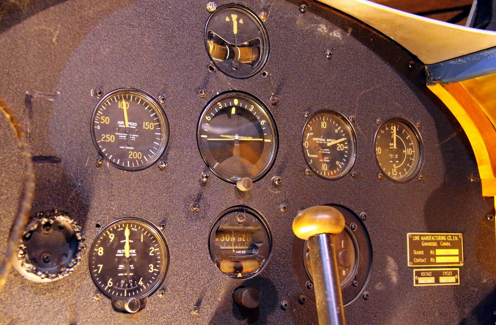 Link Trainer
- letecký trenažér / Kanada 1940.
V trenažéru jsou umístěny ovladače přípusti motoru,držák palubních hodin, ruční a nožní řízení, spojovací skříňka radia. Z přístrojů jsou vidět rychloměr, výškoměr, zatáčkoměr, umělý horizont, vodorovný kompas, variometr, ukazatel ILS, otáčkoměr. Na dalším záběru je ovládací stůl instruktora se záznamem letěné trasy.
